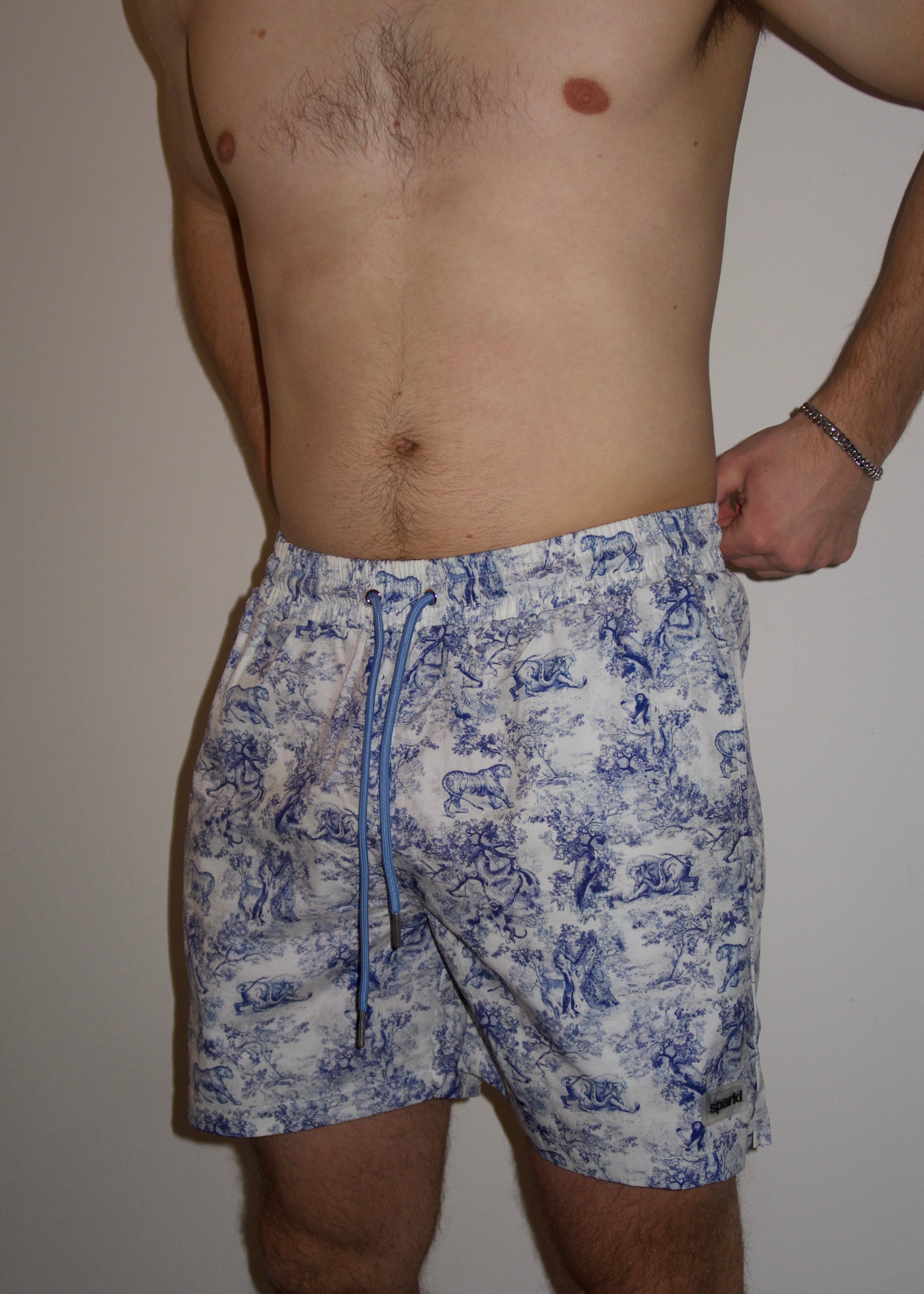 Male wearing blue and white luxury printed swim shorts with blue drawstrings and pockets