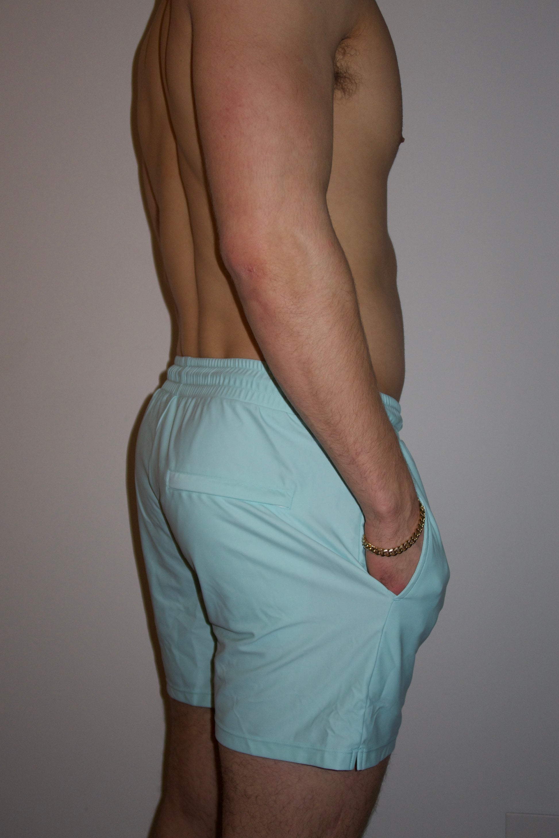 Male wearing light blue luxury swim shorts facing backward to show back and side pockets